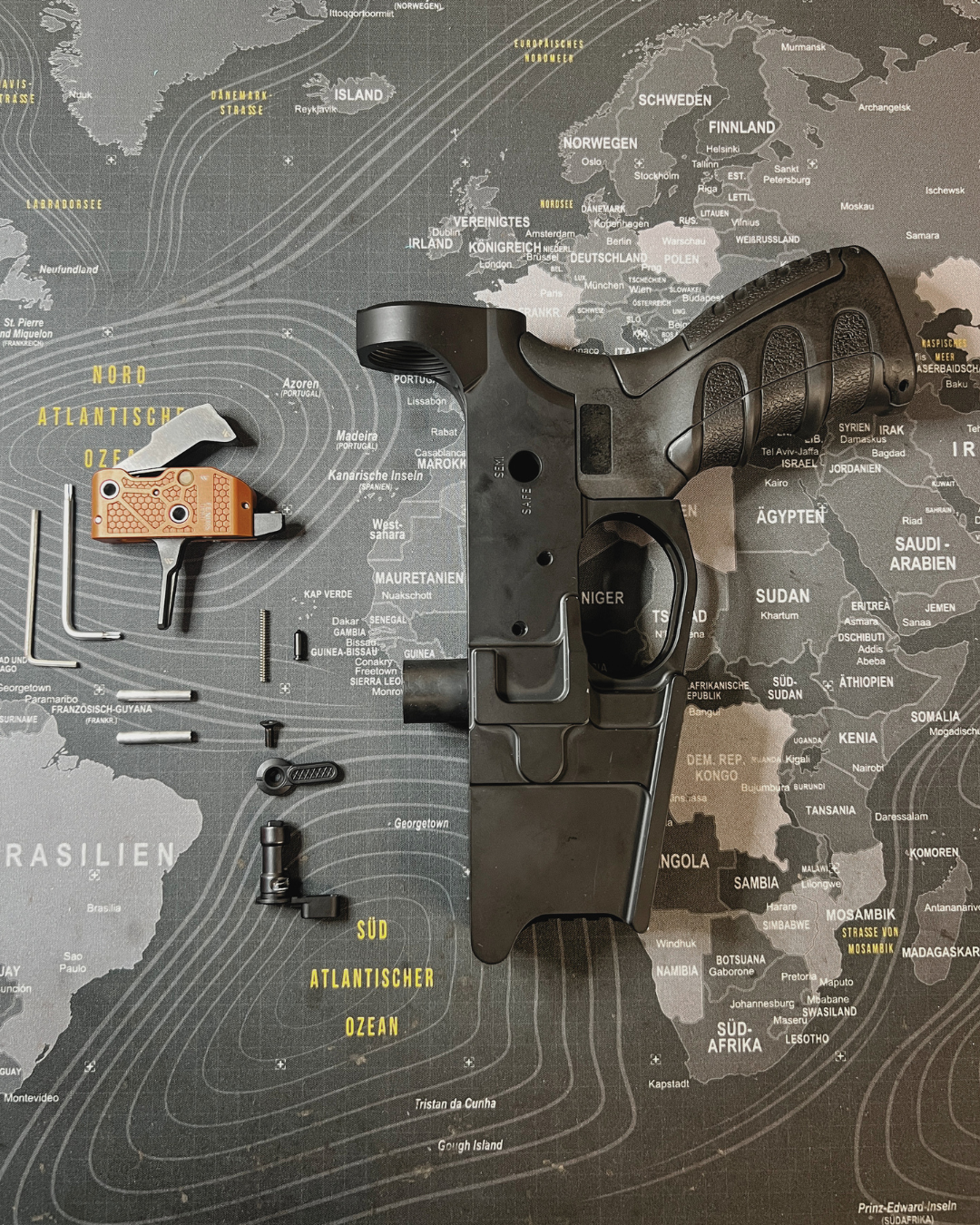 WPNTEC FENRIS Abzug Einbau – Lower Receiver mit Abzugsgruppe und Einzelteilen auf Weltkarte